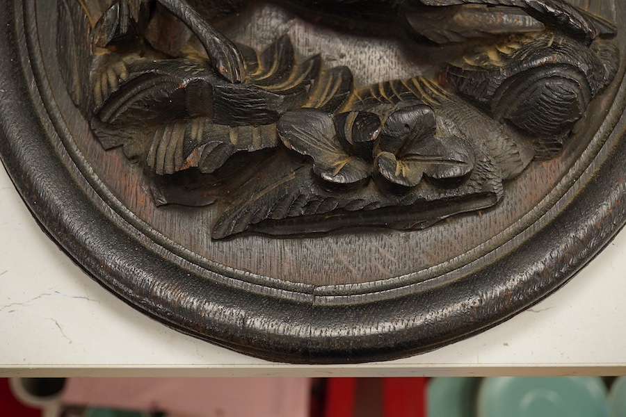 An early 20th century oval carved oak panel depicting a dog before a kennel, 46cm high. Condition - good